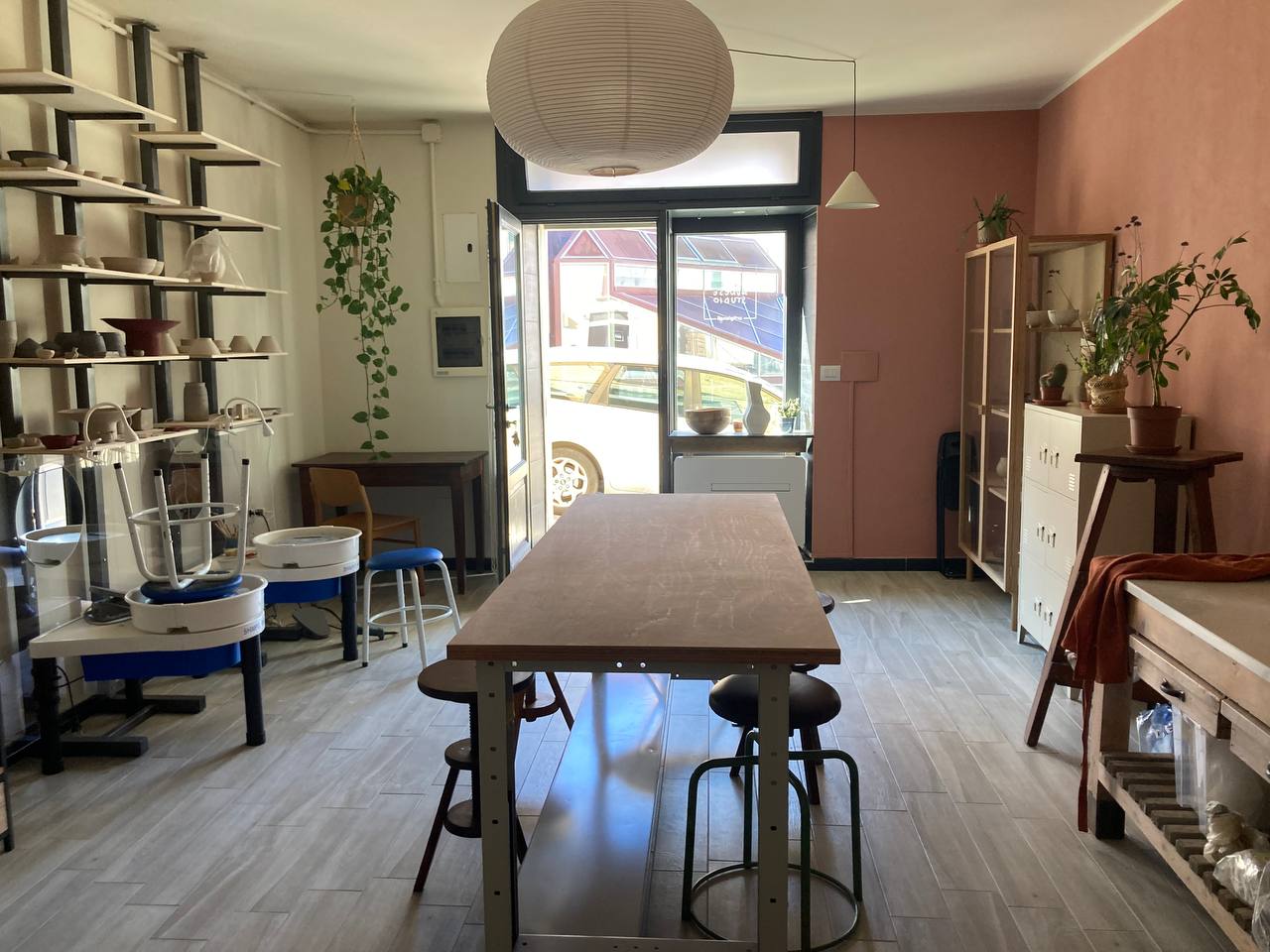 Interno dello studio di ceramica con tavolo da lavoro, tornio e scaffali con ceramiche